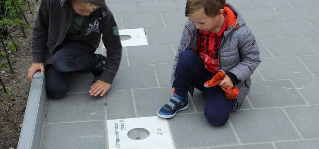 Knikkerpotje Kinderen knikkeren op schoolplein van CBS Rehoboth