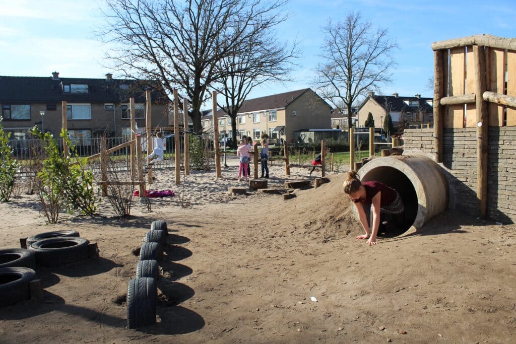 Tunnel en heuvel Meisje komt uit tunnel bij een groen schoolplein